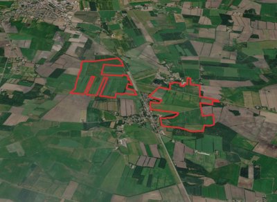 Luchtfoto van akkerland met twee rood omlijnde gebieden, met een weg en een klein dorp ertussen