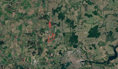 Satellite map of fields and woodland with two areas outlined in red and a town at the lower right.